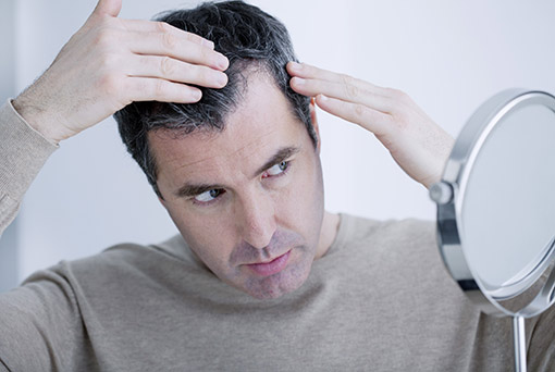 homme inspectant ses cheveux devant un miroir Calvitie chez l'homme | DHI Paris
